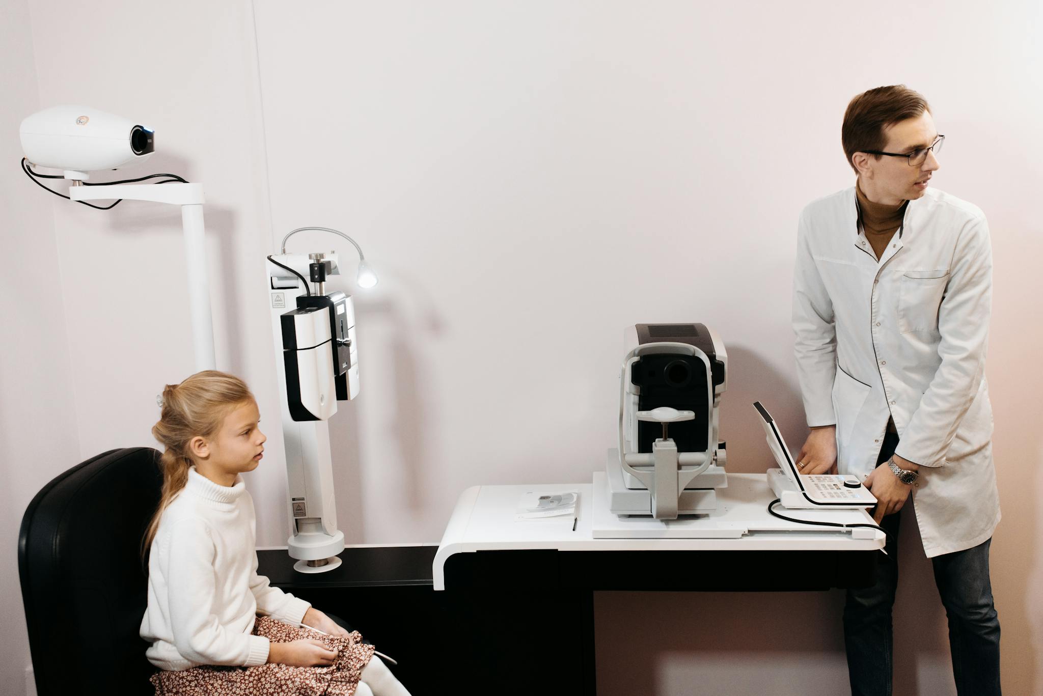 A young girl sits for an eye exam with an optometrist using digital equipment.